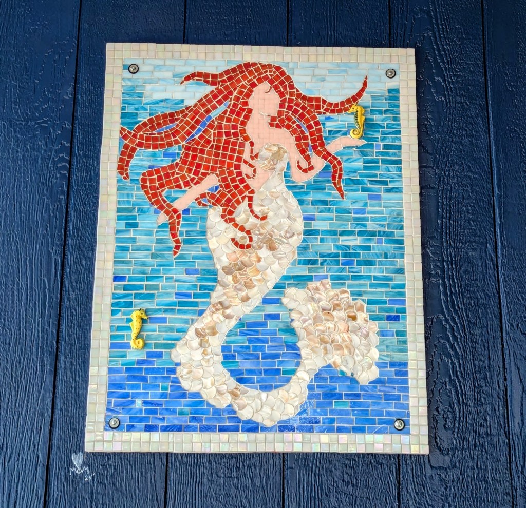 Blue mosaic mural of a red-haired mermaid holding a small seahorse.