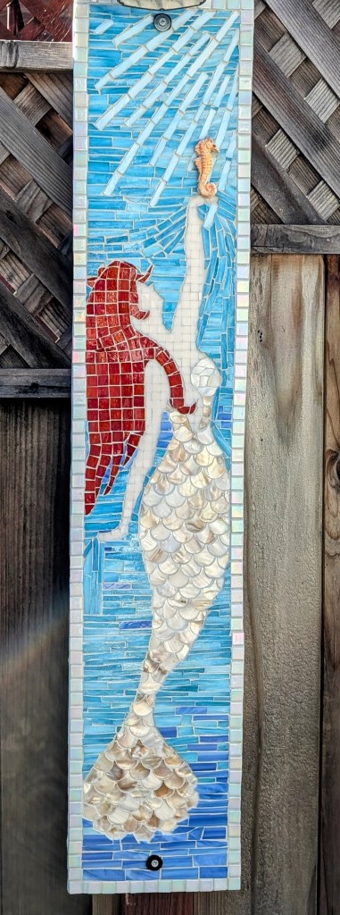 Tall mosaic mural of a red-haired mermaid reaching toward a seahorse.