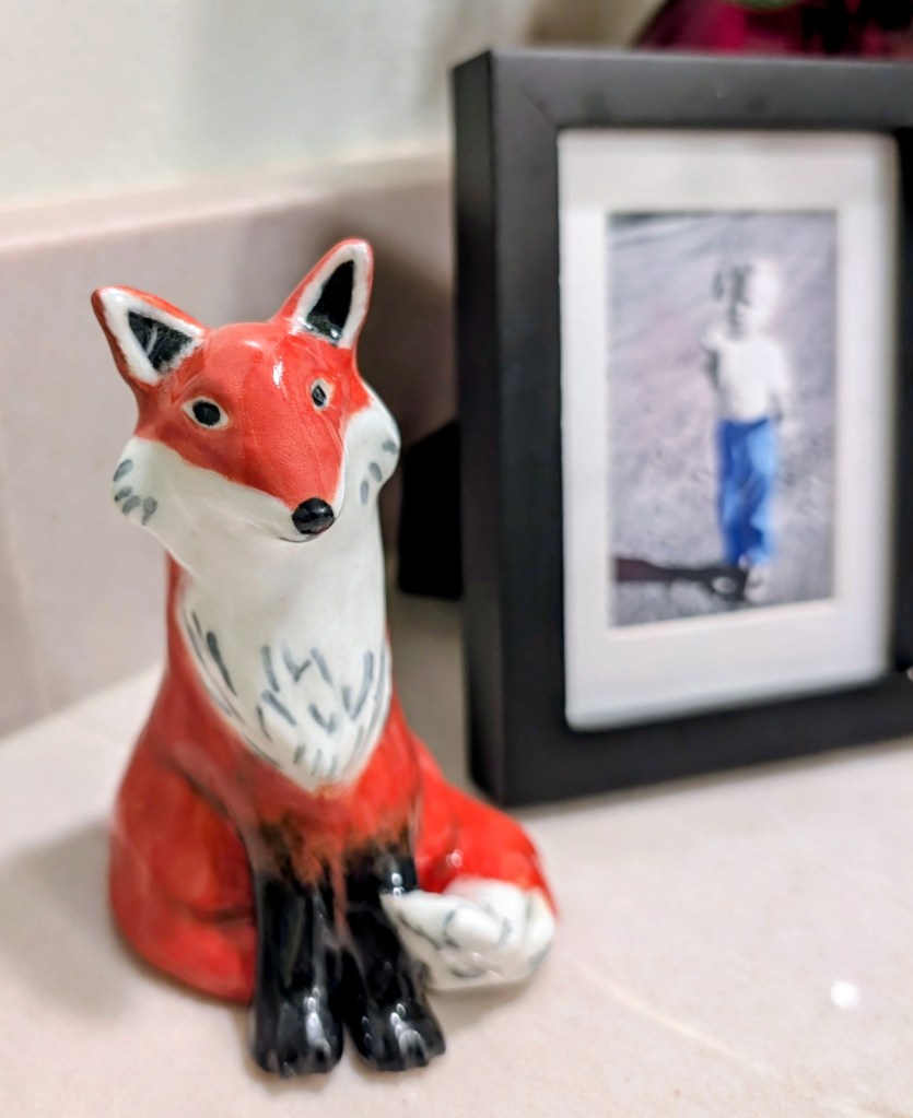 Red ceramic fox seated beside a framed photograph.