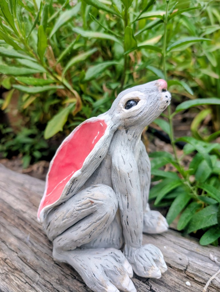 Side view of a gray ceramic bunny with a glossy pink ear.