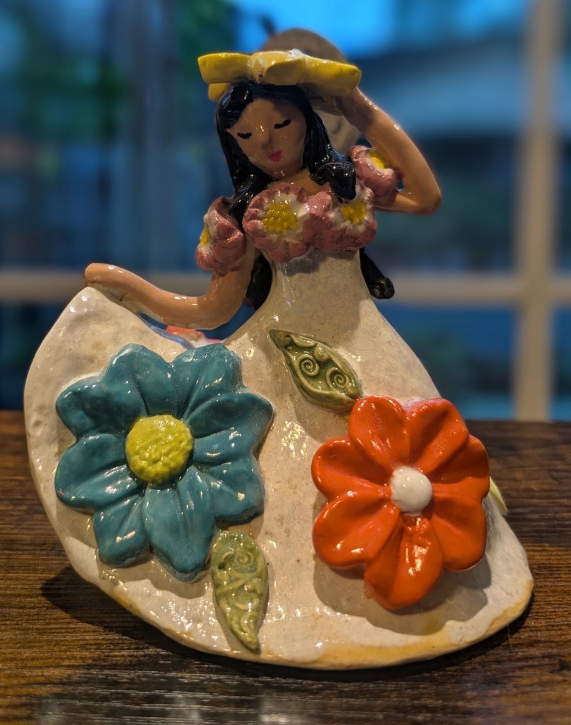 Ceramic Latina girl in a flower-covered dress holding a yellow hat.